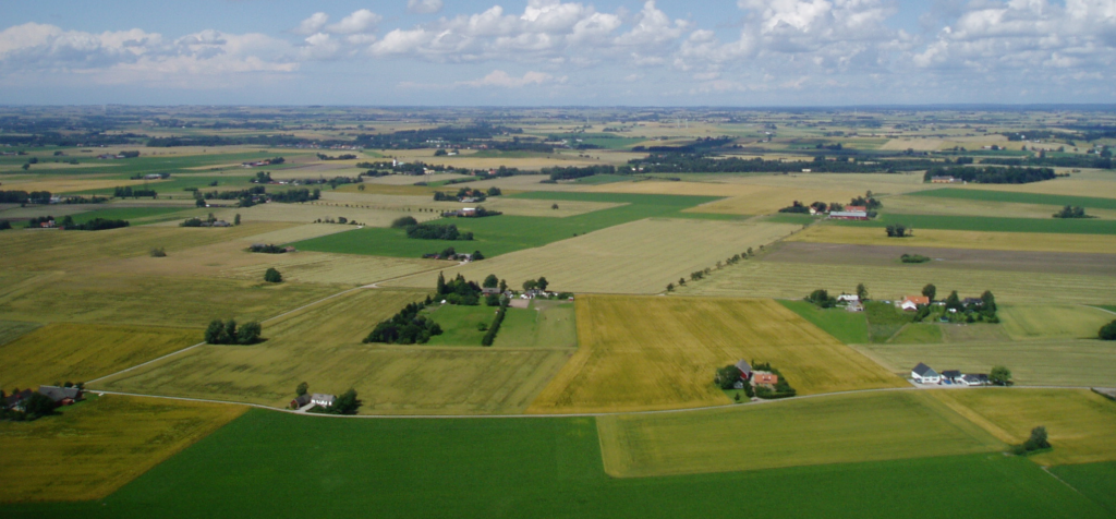 Flygfoto som visar skånska åkrar och gårdar som ett lapptäcke