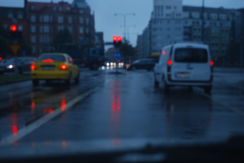 Bilar sedda bakifrån i stadstrafik. Det är skymning och regnfuktigt.